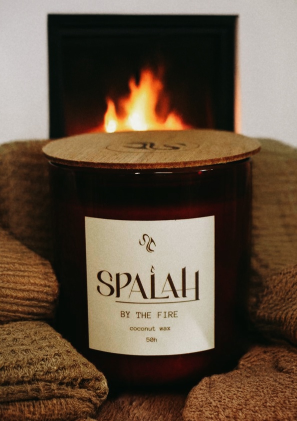 Dark candle 'By The Fire' next to a crackling fireplace